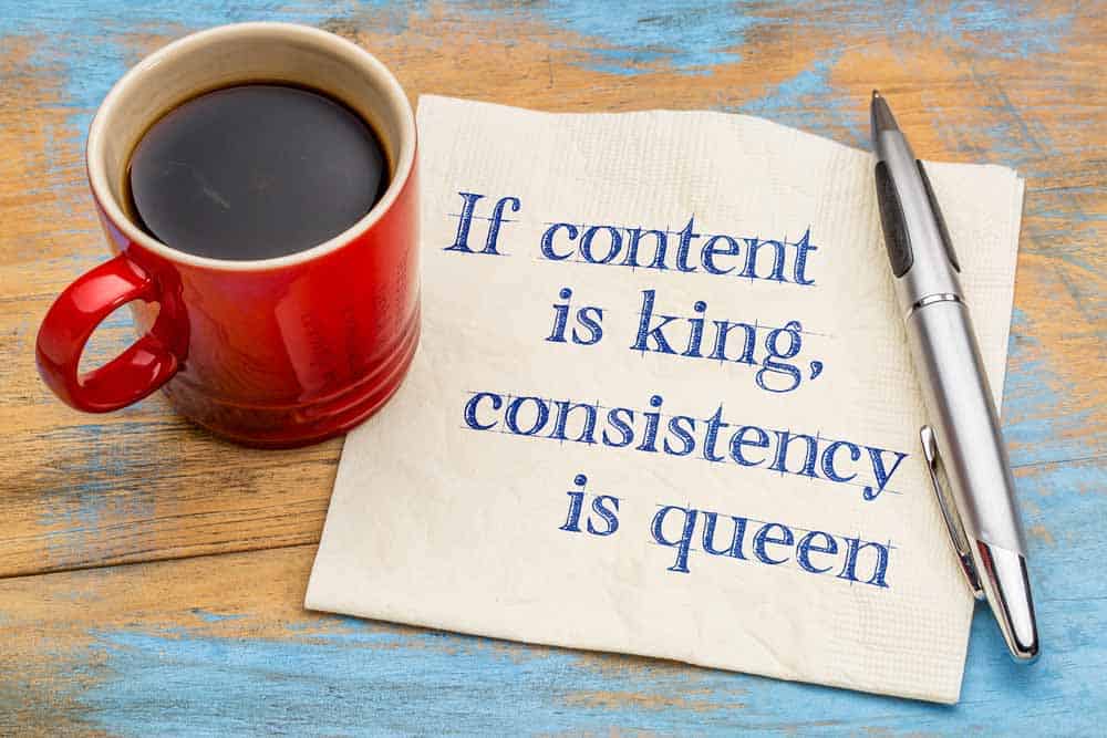 Pen, napkin and cup of coffee on an old table, with words written on napkin "if content is king, consistency is queen"