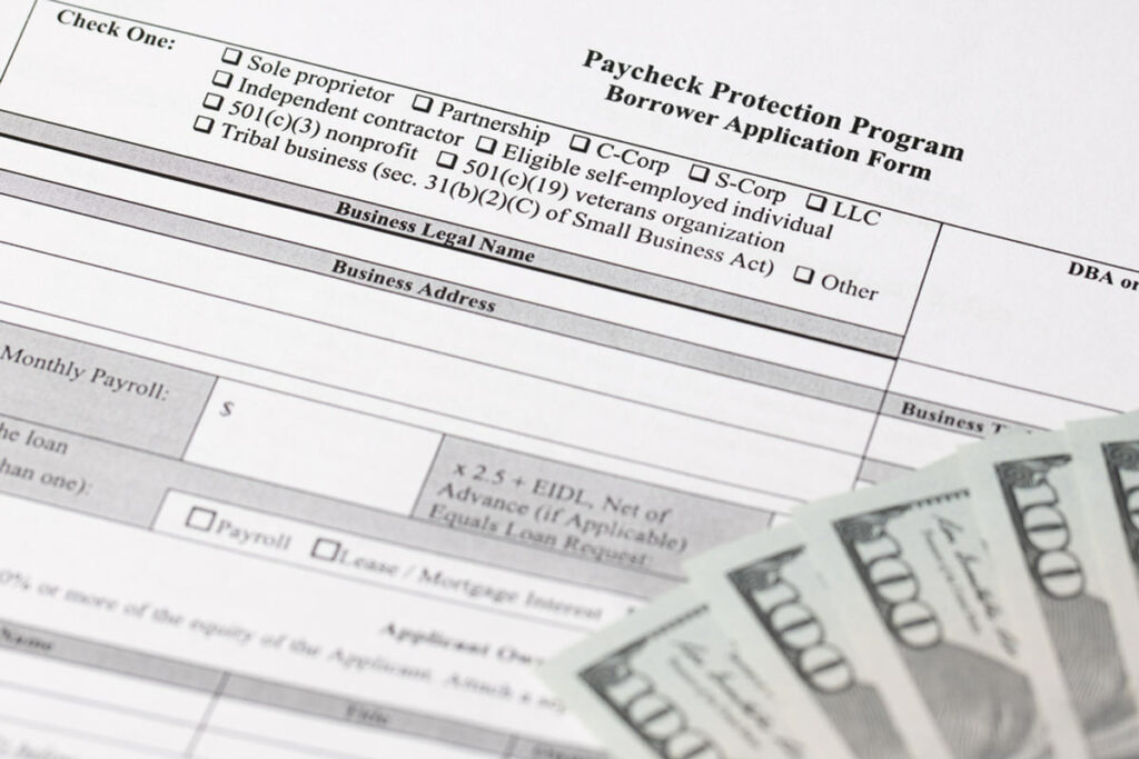 Paycheck protection program application form with several $100 dollar bills laid out on the side.