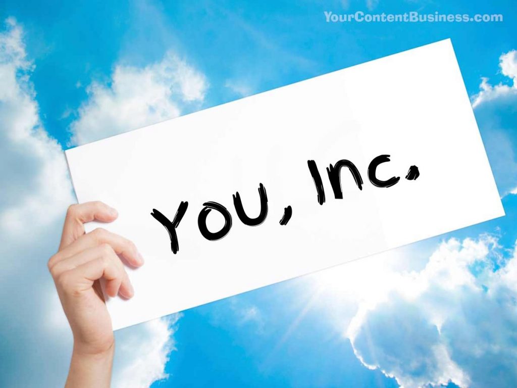 A hand holding up a sign against a partly cloudy sky with the words "You, Inc." hand written with a black marker.