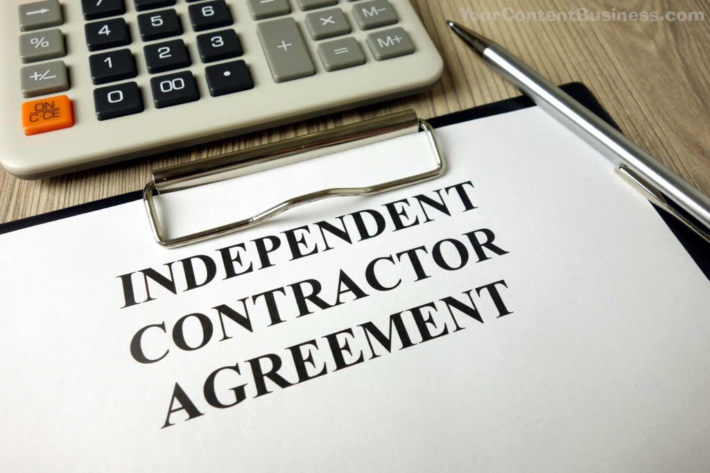 A calculator, a clipboard and a pen sitting on a woodgrain table, and attached to the clipboard is a document entitled Independent Contractor Agreement.